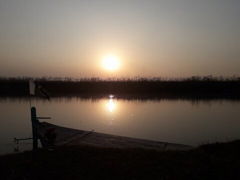 Golden Sunset Reflecting on Calm Water with a Silhouetted Traditional Wooden Boat on the Shore - Powered by Adobe