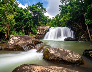 A serene waterfall cascades over rocks into a calm pool. Lush green trees frame the scene under a partly cloudy sky