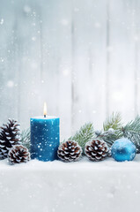 Blue Christmas candles, balls and pine cones in a row with spruce branches covered with snow and snowfall on white wooden board background in winter.