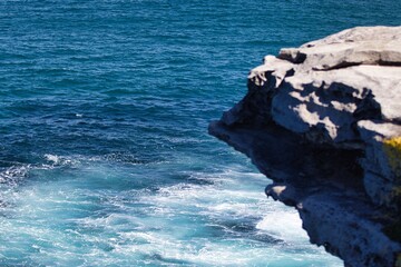 Dramatic seascape with towering rocky cliffs overlooking the crashing azure waves of the ocean below.