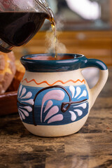 Hot coffee steaming in a traditional artisanal mexican pottery mug with concha bread