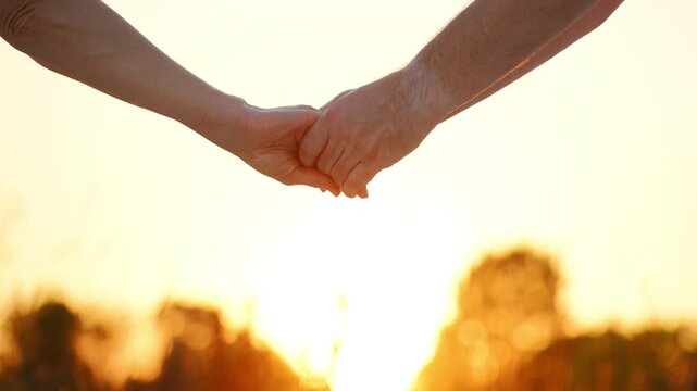 Four silhouetted hands of men and a women against a warm sunset, creating a scene that symbolizes love, family, support, unity. Background is blurred landscape with soft light
