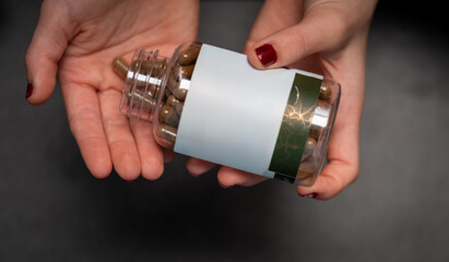 Close-up of female hands holding a glass bottle with dietary supplement capsules. Concept of wellness, health care, vitamins, and daily natural nutrition routine.