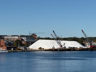 Massive salt pile covered by white tarp with cranes and construction vehicles at harbor waterfront of Portsmouth, New Hampshire