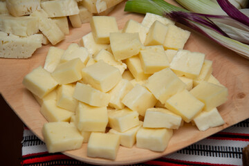 a pile of cheese cubes on a wooden board. They appear to be a type of hard cheese, possibly cheddar.