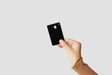 Hand holding a black plastic bank card on a gray background	
