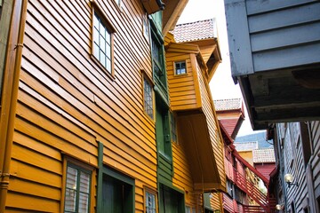 Colorful, weathered wooden buildings line a quaint alley in a historic Norwegian town, creating a...