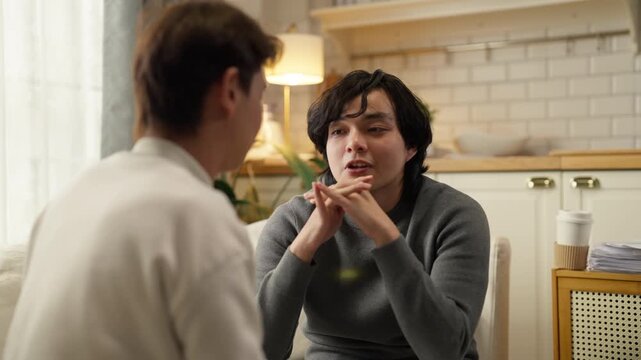 Asian gay male couple experiences relationship conflict during serious discussion on living room sofa at home daytime, working through disagreement and communication challenges to strengthen their par