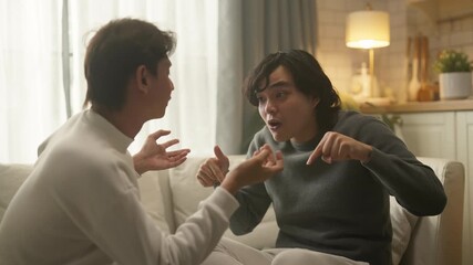 Asian gay male couple experiences relationship conflict during serious discussion on living room sofa at home daytime, working through disagreement and communication challenges to strengthen argue - Powered by Adobe