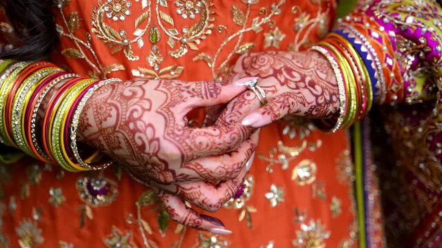 Close up view of Traditional Indian or Pakistan henna painted bridal hands with wedding rings. Bride adjusting her rings and bangles on the hands