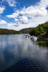 Serene lake nestled in lush forest under a picturesque cloudy sky, with scenic boats docked along the shoreline.
