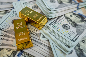 Shiny gold bullion bars on hundred dollar banknotes representing luxury, savings and financial...