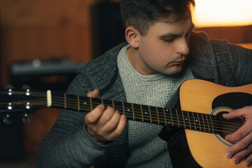 Obraz premium Young man playing acoustic guitar in cozy indoor setting, focusing on music and creativity, with warm lighting and relaxed mood