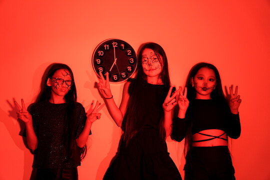 The three figures, dressed for Halloween, stand and sit in a dimly lit room