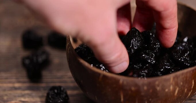 black prunes made from ripe blue plums in a coconut shell plate, dried plums in a bowl