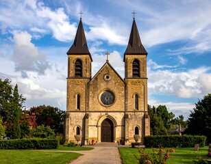 Fototapeta premium A symmetrical stone church, flanked by twin towers, stands against a blue sky with scattered clouds. A pathway leads to the entrance
