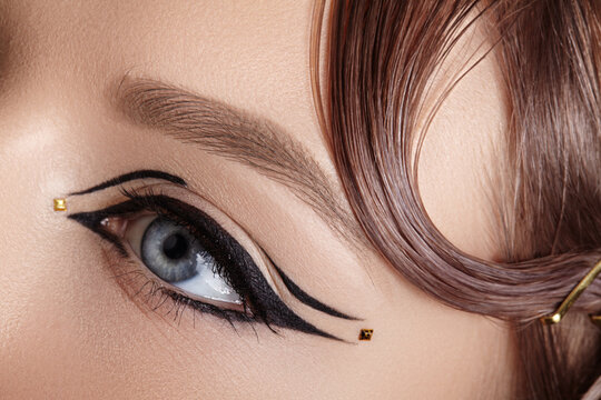 Artistic eye makeup featuring bold black winged eyeliner and small gold dots, emphasizing creativity and high-fashion beauty expression. Macro close-up Beauty for cosmetic brands, make-up artist