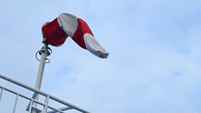 Red and white wind direction indicator cone flag during heavy weather, showing wind direction and waving and changing direction fast and strongly. 