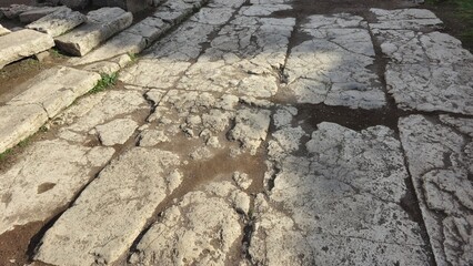 Rome, Italy - 13 January 2025. Fragmented stone roadway with deep cracks and weathered surfaces lies within the Roman Forum, bordered by steps on the left.