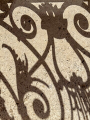 Ornamental Ironwork Shadow on Light Stone Surface with Elegant Curved Patterns