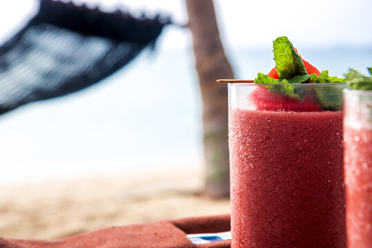 Red smoothie tropical cocktail in glass jar with mint leaves at beach restaurant with sea and hammock on background as vacation lifestyle