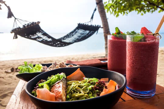 Served table with European cuisine and tropical cocktails at beach restaurant with sea and hammock on background as vacation lifestyle