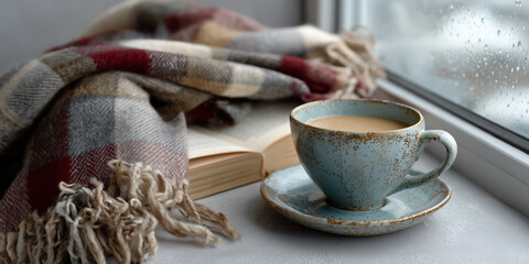 Cozy morning by the window with a cup of warm coffee, a soft blanket, and an open book on a rainy day