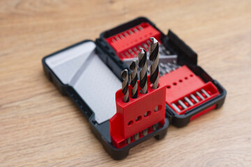 Close-up of a metal drill bit set organized in plastic case on wooden table. Concept of tools,...