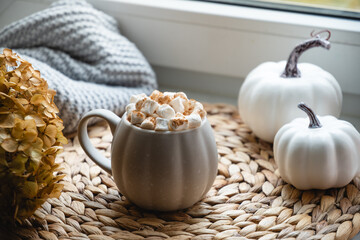Autumn warming chocolate or coffee with marshmallows, pumpkins and candle on window sill. Season beverage. Close up.