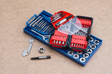 Metal thread cutting tap and die set with handle, drill bits, and gauges arranged on a wooden...