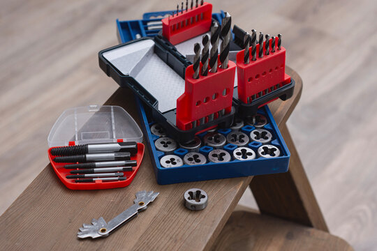 Metal thread cutting tap and die set with handle, drill bits, and gauges arranged on a wooden workbench. Industrial mechanic tools for metalworking, threading, repair and engineering work.
