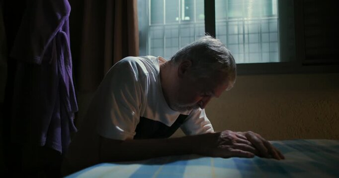 Elderly man leaning forward on bed with head down reflecting in quiet solitude introspective moment of thought calm serene atmosphere of reflection