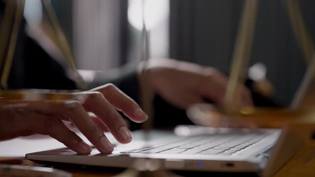A person is typing on a laptop. The person is wearing a black shirt. The laptop is on a wooden table