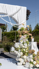 elegant outdoor wedding arch on the podium with fabric, beads, candles, layers and romantic floral arrangement in white and green tones. Amaranth, anthurium, hydrangea, rose, dahlia. Summer atmosphere