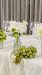 wedding decoration of the bride's table. Flower arrangement in white and green colors, vases with flowers, white tablecloth, necklace. Rose, chrysanthemum, dahlia, grapes, hydrangea, anthurium