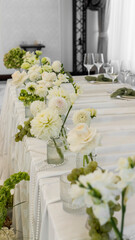 wedding decoration of the bride's table. Flower arrangement in white and green colors, vases with flowers, white tablecloth, necklace. Rose, chrysanthemum, dahlia, grapes, hydrangea, anthurium