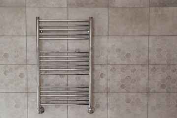 A chrome towel warmer on a tiled wall in a bathroom.