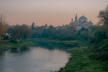 Scenic view of a historic Russian town with churches and domes near a calm river at sunset. Peaceful autumn landscape with pastel sky and soft natural light.