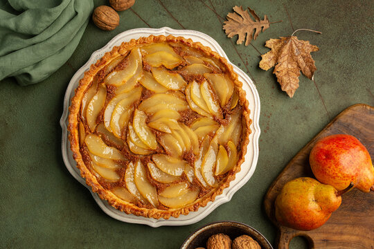 French poached pear tart, made with a sweet frangipane, almond and wallnuts cream. Green table with autumn decoration.  Autumn, Thanksgiving  dessert.