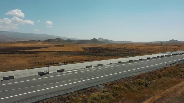 Aerial drone shot of cars driving on a newly constructed highway section through a vast, dry steppe landscape. Infrastructure project, travel, and road repair footage.