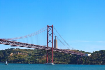 View of famous Lisbon bridge over Tagus river with Jesus Christ statue standing on the hill
