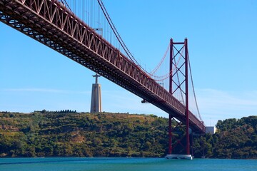 View of famous Lisbon bridge over Tagus river with Jesus Christ statue standing on the hill