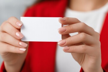 Obraz premium A woman with manicured nails displays a blank card in her hands. She is dressed in a red jacket and is in a contemporary environment. The focus is on her confident posture