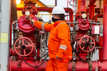 Technician in orange uniform inspects red fire suppression system valves for safety maintenance