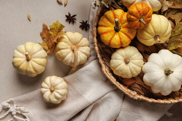 White and orange pumpkins in woven basket surrounded by dry leaves, cardamom and star anise on soft fabric..