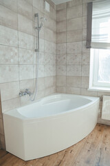Corner acrylic bathtub with plastic front panel underneath in a bathroom with a window