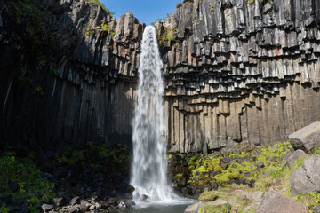 Majestic waterfall cascading down rocky cliffs surrounded by lush greenery, showcasing the beauty...