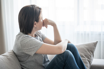 Sad girl sits on the sofa at home, problem concept