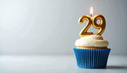 Cupcake celebrates twenty ninth birthday with burning candle. Golden number 29 on cake with white cream in blue wrap. Festive baked dessert for anniversary party celebration.
