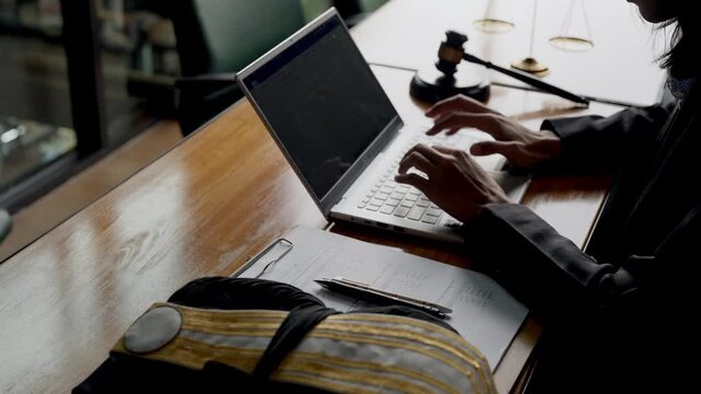 Young female lawyer managing legal work on laptop with documents, gavel, and justice scale.